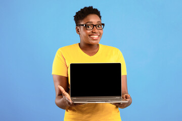 Poster - Smiling Oversized Black Woman Holding Laptop With Blank Screen Posing Over Blue Studio Background. Lady Showing Computer Monitor Recommending Website. Mockup