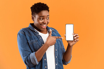 Poster - Cheerful Black Lady Showing Smartphone Blank Screen Recommending Application Posing Standing Over Yellow Studio Background. Mobile Application Ad. Check This App Concept. Mockup