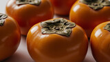 A close-up captures a group of vibrant orange persimmons, each featuring its distinctive green calyx, set against a soft, blurred background.