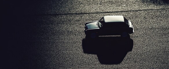 Wall Mural - vintage car driving on asphalt road with dramatic lighting and shadows in urban setting