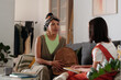 © pressmaster - Young adult Hispanic woman sitting on sofa helping Caucasian girl prepare for school, holding backpack while girl holding notebook, both engaged in conversation indoors