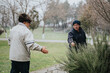 © qunica.com - Two senior men are seen in a park setting, one handing an item to the other with light snow falling around, creating a serene and friendly scene.