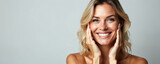 Middle aged blonde woman smiles holding hands near face. Happy, positive, well-groomed model with healthy skin. Beautiful white teeth. Portrait beauty photo. Isolated on grey background. Skincare