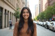 © Vadym - Young hispanic woman smiles in urban cityscape. Beautiful brunette with long hair, cheerful expression. Happy female stands outdoors on sunny day. Confident woman enjoys lifestyle in modern city,
