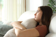 © PheelingsMedia - Apathetic woman hugging pillow on a sofa at home