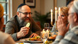 © Julian - Mature Jewish man with piece of fresh cucumber in hand looking at guest or family member during chat by Hanukkah dinner