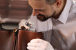 © New Africa - Appraiser with loupe evaluating leather bag indoors