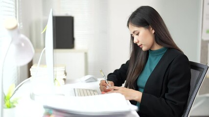 Aufkleber - Professional businesswoman carefully writing notes on a notepad while sitting at desk, wearing teal turtleneck and black jacket, focusing on workplace task with concentrated efficiency