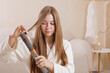 © st.kolesnikov - Woman styling long hair with a modern curler at home, beauty care, healthy hair, technology, smooth hairstyle, selfcare routine.