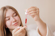 © st.kolesnikov - Woman using a dropper to apply red facial serum, focusing on skincare, hydration, anti-aging, and modern beauty routine for glowing skin.