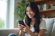 © Sync - Happy woman using smartphone at home, online shopping, natural light