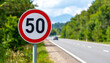 © hardvicore - Traffic sign 50 km h maximum, speed limit for speeding vehicles. Blurred natural backdrop.