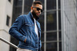 © Dmytro Hai - Stylish black man in sunglasses holding hands in pockets of denim jacket on street