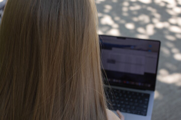 Poster - A woman is sitting on a bench with a laptop open in front of her. She is looking at the screen, possibly working or browsing the internet. Concept of productivity and focus