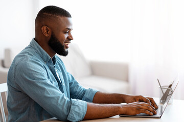 Aufkleber - Smiling Millennial African American Man Working With Laptop At Home Office. Handsome Black Self-Employed Guy Typing On Laptop Keyboard, Positive Male Freelancer Sitting At Desk, Side View, Copy Space