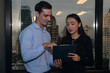 © S photographer - Two professionals collaborating on a digital tablet, discussing ideas in a modern office setting with city skyline view.