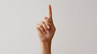 © Curioso.Photography - Female hand with raised index finger pointing upward against a neutral background.