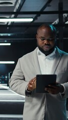 Poster - Vertical video Server room technician doing troubleshooting using tablet to prevent downtime. IT expert walking in data center checking network performance metrics and security logs using device
