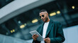© Favio - Young african american man in casual business attire using a tablet outdoors near a contemporary building.
