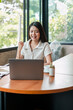 © Satori Studio - A young woman engaged in remote work on her laptop at a modern cafe, surrounded by natural light and greenery.