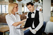© Seventyfour - Caucasian middle aged woman showing laptop screen to Caucasian young adult man in waiter uniform standing in restaurant interior discussing work related information