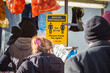 A sign requesting social distancing and maintaining a 2-meter distance is visible as unidentified people shop at a outdoor market in Wood Green, London, England