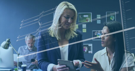 Poster - Reviewing tablet, women in business attire collaborating in office with charts and digital overlay