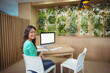 © WavebreakMediaMicro - Adult woman sitting at wood desk in workspace with plant wall, facing blank monitor, copy space