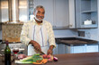 © wavebreak3 - Senior African American man chopping vegetables on wooden cutting board in kitchen with wine bottle