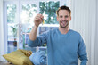 © WavebreakMediaMicro - Man standing in living room holding house keys and smiling near potted plants, copy space