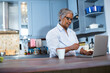 © wavebreak3 - Senior African American woman checking credit card at kitchen counter using laptop with white mug