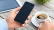 © Koplexs-Stock - Hand holding smartphone next to coffee cup and tablet on wooden surface.