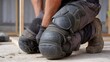 © Devian Art - A construction worker kneeling with knee pads and work boots on a concrete surface indoors