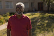 © WavebreakMediaMicro - African American senior man standing in sunlit front yard wearing red polo shirt and eyeglasses