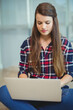 © WavebreakMediaMicro - Woman sitting cross-legged on floor working on silver laptop in modern office with glass panels