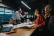 © qunica.com - A diverse group of professionals actively participating in a dynamic business meeting. They are working together, sharing ideas and strategies around a table with laptops and documents.