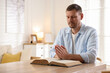 © New Africa - Man with Bible praying at table indoors. Space for text