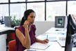 © Wavebreak Media - Senior woman writing notes in open notebook at open-plan office desk with headset and monitor