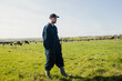 © Wavebreak Media - Male farmer standing wearing coveralls and boots in pasture watching grazing cows across fence