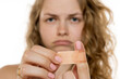 © vladimirfloyd - Woman looking frustrated, holding adhesive bandage with a focused expression. Blurred background suggesting minor injury or discomfort