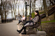 © Albert - Side view of pleased brunette woman sitting on bench in park and using phone