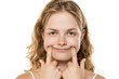 © vladimirfloyd - Young woman with wavy blonde hair forcing a smile by pushing her cheeks with fingers, demonstrating fake emotions against white background