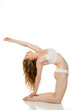 © vladimirfloyd - Young woman with wavy blonde hair in white underwear performing advanced yoga backbend pose, demonstrating flexibility and strength against white background