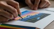 © ajib ajib - Person drawing a colorful mountain landscape with colored pencils on a sketchbook