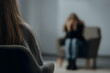 © Health Studio - Two women in a counseling session, one in focus with her back to the camera, the other blurred and sitting on a couch, conveying emotional support and therapy.