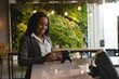 © Wavebreak Media - African American woman wearing blazer using POS terminal at marble counter in cafe with plant wall