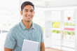 © Wavebreak Media - Indian man smiling while holding laptop near office shelves with plant and box, copy space