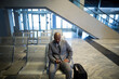 © Wavebreak Media - African American man in suit sitting at escalator in airport holding smartphone before glass doors