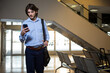 © Wavebreak Media - Man wearing shirt and trousers walking in airport terminal holding smartphone and carrying bag