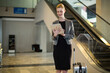 © Wavebreak Media - Businesswoman standing in airport terminal reading tablet beside rolling suitcase and escalator